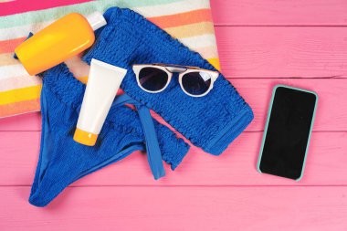 Parlak pembe ahşap arka planda güneş kremi şişeli mavi bikini.