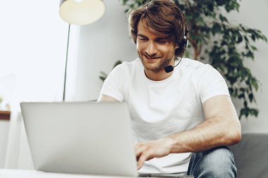 Kulaklıklı genç bir işadamı evden bilgisayarda çalışıyor.