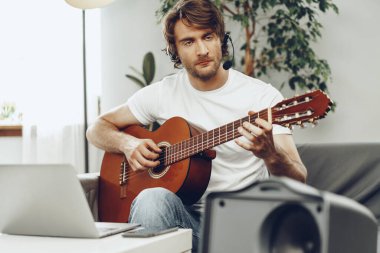 Genç adam dizüstü bilgisayarında gitar dersi izliyor.