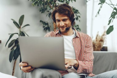 Kulaklık takan genç adam laptopla video görüşmesi yapıyor.