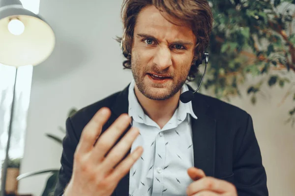 Close up portrait of an angry businessman with headset having stressful online conversation — Stock Photo, Image