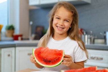 Küçük kız mutfakta karpuz yiyor.