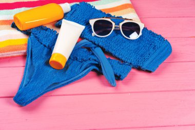 Parlak pembe ahşap arka planda güneş kremi şişeli mavi bikini.