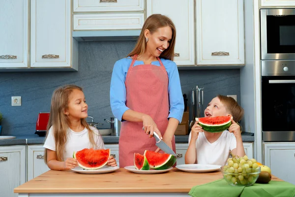 Zoet familie, moeder en haar kinderen eten watermeloen in hun keuken hebben plezier — Stockfoto