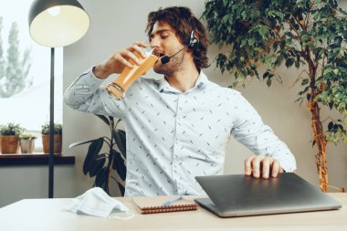 Sakallı adam bir bardak bira içerken dizüstü bilgisayarını kullanıyor.