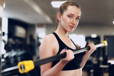 Spor salonunda halterle egzersiz yapan esmer, genç bir kadın.
