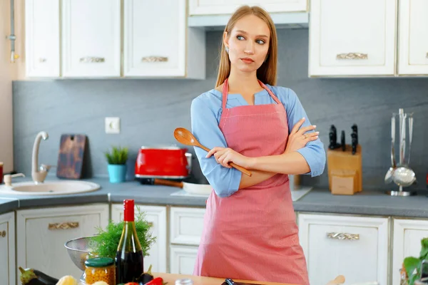 Atractiva joven en delantal rojo de pie en su cocina —  Fotos de Stock