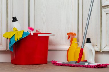 Yerdeki plastik kovada çeşitli ev temizlik deterjanları ve şişeleri.