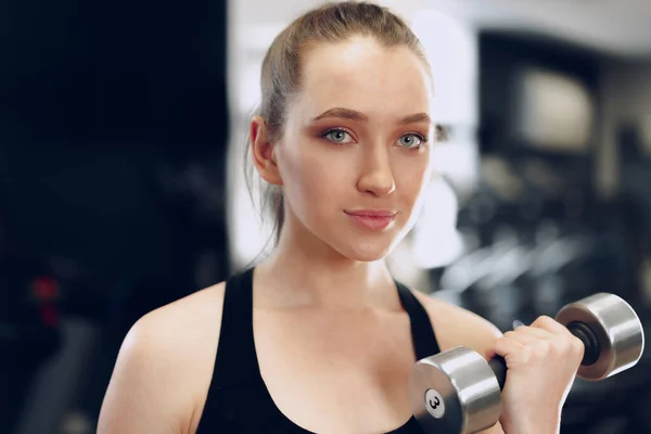 Joven morena deportista haciendo ejercicio con la mancuerna en un gimnasio — Foto de Stock