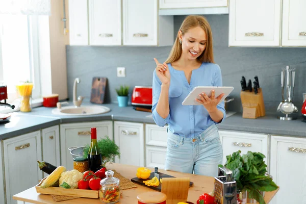 Joven hermosa mujer caucásica cocinar y el uso de su tableta digital en la cocina —  Fotos de Stock