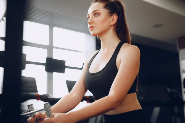 Ελκυστική νεαρή γυναίκα κάνει ασκήσεις για τους μυς των χεριών και πίσω σε ένα γυμναστήριο — Φωτογραφία Αρχείου