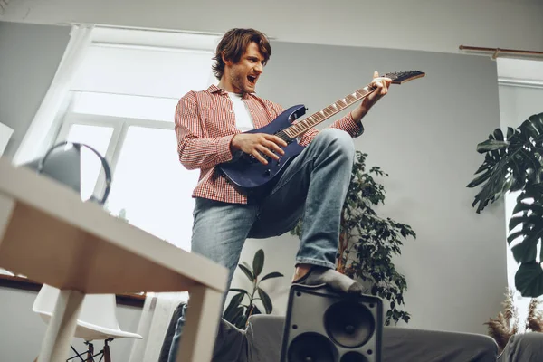 Young man plays guitar and sings a song at home with electric guitar