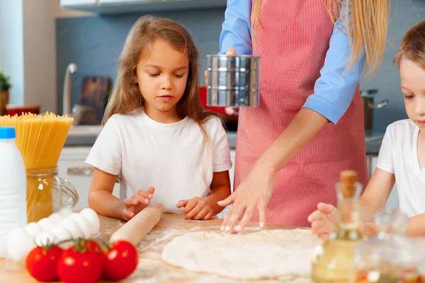 Genç sarışın kadın, anne ve çocukları hamur pişirirken eğleniyorlar.