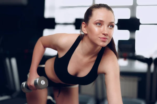 Jovem morena esportiva mulher exercitando com halteres em um ginásio — Fotografia de Stock