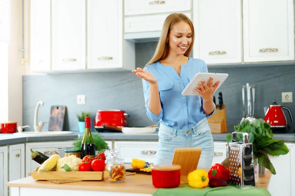 Jovem bela mulher caucasiana cozinhar e usar seu tablet digital na cozinha — Fotografia de Stock