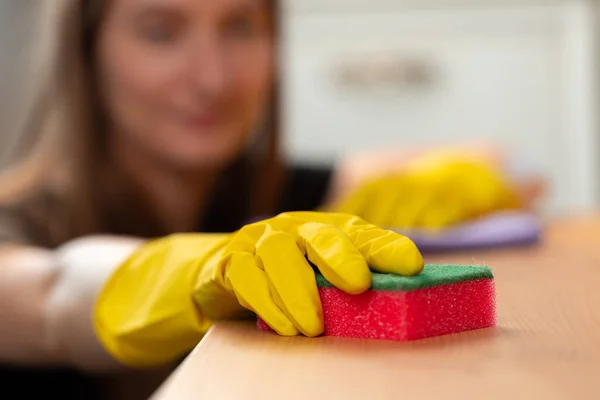 Unrecognizable woman in yellow gloves wiping wooden table top — Stock Photo, Image