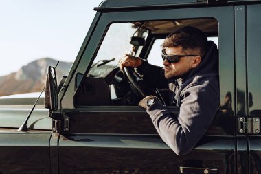Bir off-road aracının erkek sürücüsü camdan içeri bakıyor.