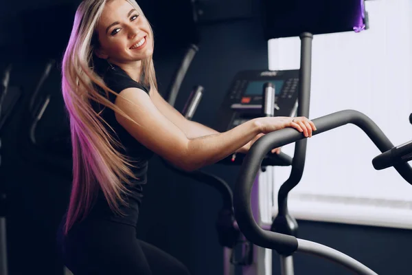 Jeune femme blonde attrayante faisant de l'exercice sur un appareil d'entraînement cardio — Photo