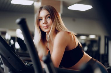 Spor salonunda kardiyo alanında antrenman yapan kıvrımlı, genç sarışın bir kadın.