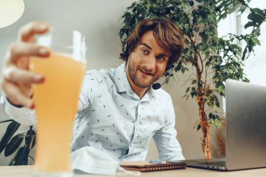 Sakallı adam bir bardak bira içerken dizüstü bilgisayarını kullanıyor.