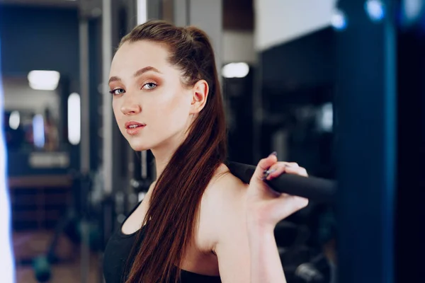 Young woman doing squats with barbell in a gym apparatus