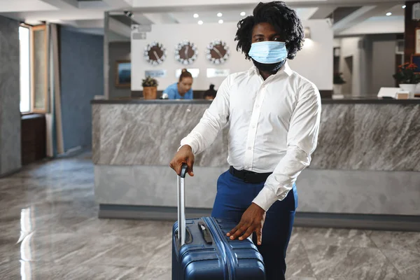 Αφρικανός φιλοξενούμενος ξενοδοχείου με βαλίτσα φορώντας προστατευτική μάσκα για προστασία από τον κορωναϊό — Φωτογραφία Αρχείου