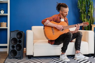 Genç stil sahibi müzisyen dairesinde gitar çalıyor.