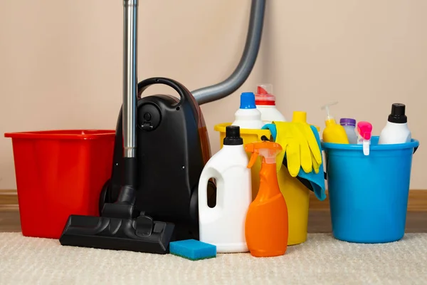 Red vacuum cleaner and plastic bucket with liquid detergents on beige carpet — Stock Photo, Image