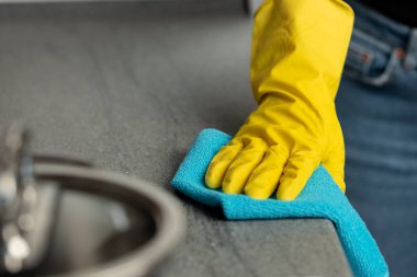 Kadınların elleri sarı eldivenlerle mutfakta tezgahı temizliyor.