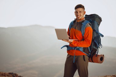 Genç adam dağ yolculuğunda dizüstü bilgisayarını kullanıyor.