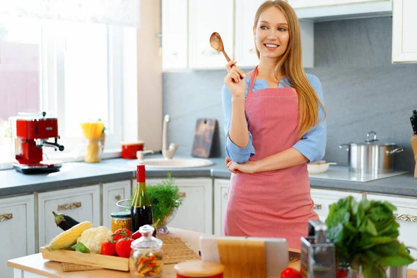 Atractiva joven en delantal rojo de pie en su cocina —  Fotos de Stock