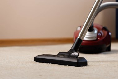 Bej bir halıda kırmızı elektrik süpürgesi