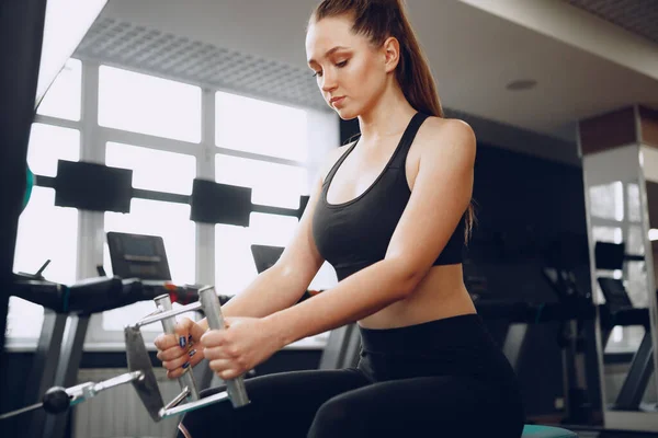 Attraente giovane donna che fa esercizi per i muscoli delle braccia e schiena in una palestra — Foto Stock