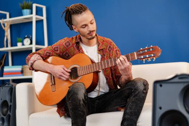 Genç stil sahibi müzisyen dairesinde gitar çalıyor.