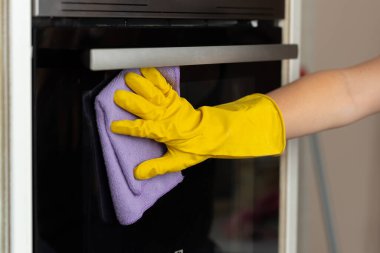 Kadın eli sarı eldivenli fırının kapağını temizler.