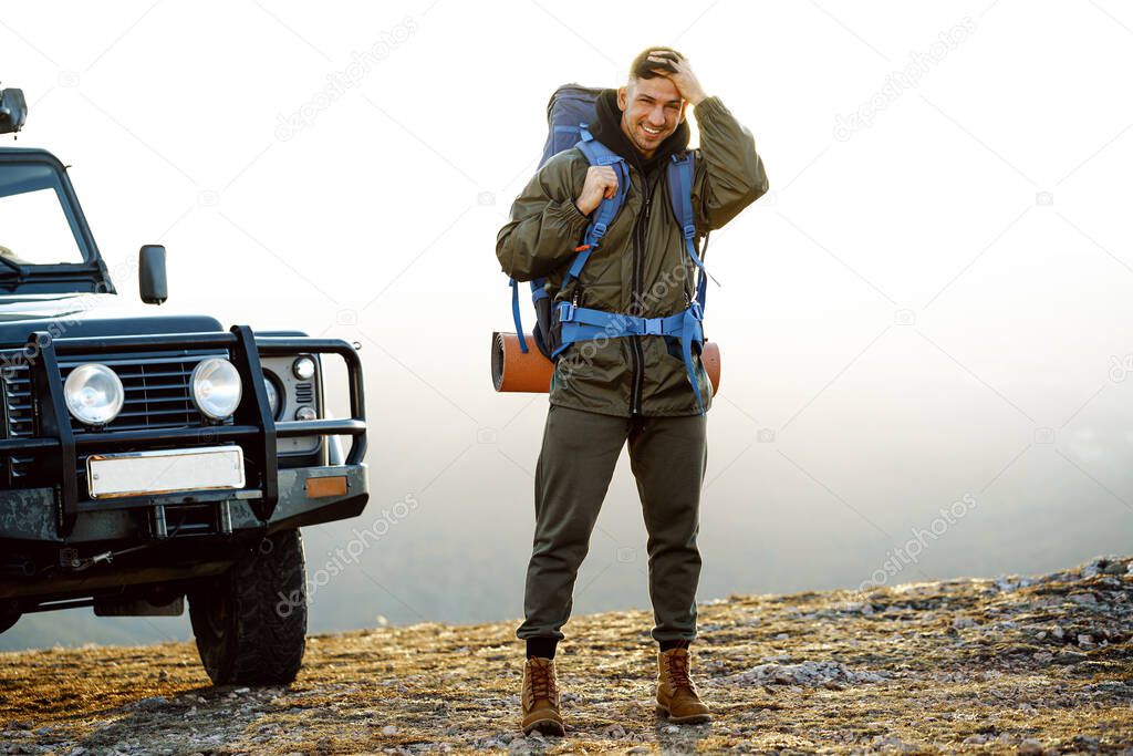 Portrait of a young traveler man in hiking equipment standing near his off-road car