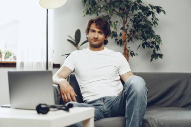 Rahat bir adam kanepede oturup kameraya bakıyor.