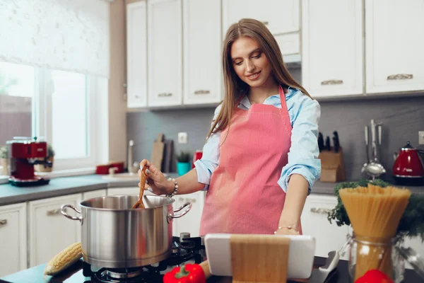 Bonita jovem cozinhando algo pelo fogão em sua cozinha — Fotografia de Stock