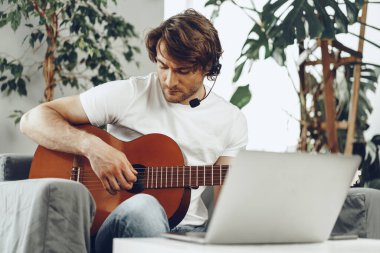 Genç adam dizüstü bilgisayarında gitar dersi izliyor.