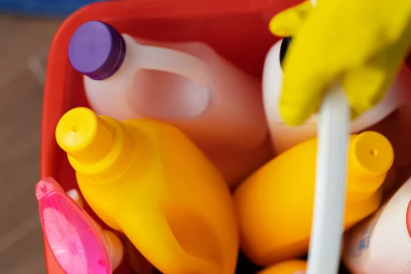 Varios detergentes y botellas de limpieza doméstica en un cubo de plástico en el suelo — Foto de Stock