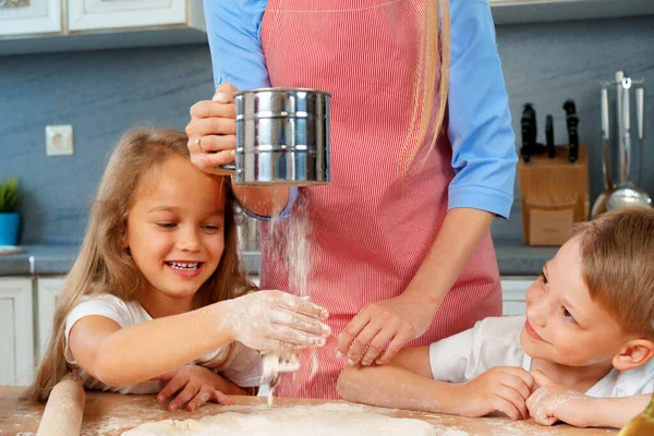 Mujer rubia joven, madre y sus hijos se divierten mientras cocinan masa — Foto de Stock