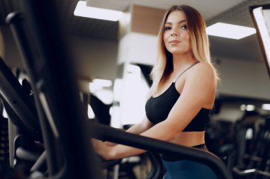 Spor salonunda kardiyo alanında antrenman yapan kıvrımlı, genç sarışın bir kadın.