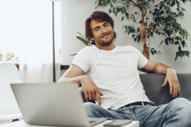 Rahat bir adam kanepede oturup kameraya bakıyor.