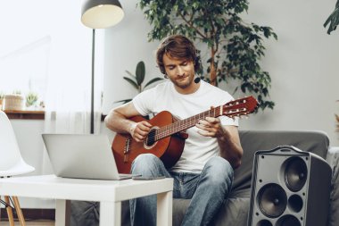 Genç adam dizüstü bilgisayarında gitar dersi izliyor.