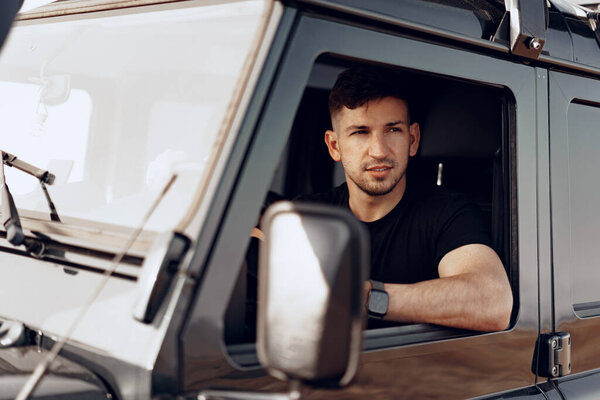 Handsome young man driver looking through the window of his off-road car