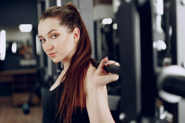 Mujer joven haciendo sentadillas con barra en un aparato de gimnasio — Foto de Stock