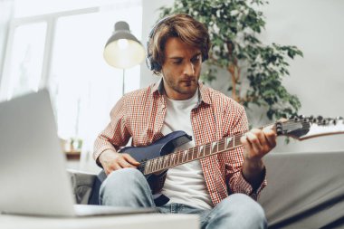 Elektro gitar çalan ve dizüstü bilgisayara müzik kaydeden adam.