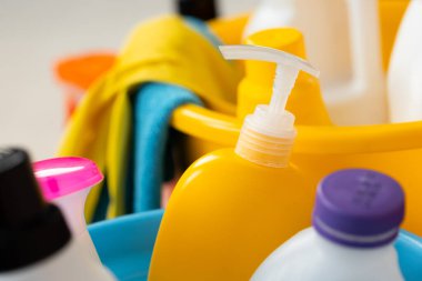 Yerdeki plastik kovada çeşitli ev temizlik deterjanları ve şişeleri.