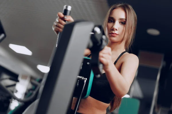 Giovane bella donna che allena le braccia in un apparato da palestra — Foto Stock