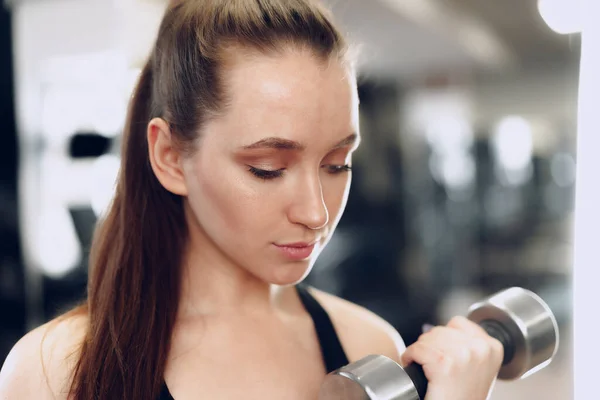 Junge brünette, sportliche Frau, die in einem Fitnessstudio mit einer Hantel trainiert — Stockfoto